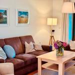 Wohnzimmer mit braunem Sofa, Holztisch und Blumen. An der Wand hängen zwei Bilder.