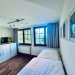 Schlafzimmer mit Bett, TV und Fenstern mit Blick auf Bäume.