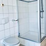 Badezimmer mit Dusche, Toilette und Toilettenpapierhalter.