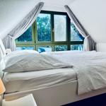 Schlafzimmer mit Dachschrägen, großem Fenster und weißem Bett.
