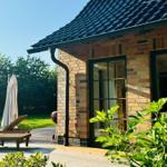 Holzterrasse mit Liegestuhl und Sonnenschirm vor einem Backsteinhaus mit Dachrinne.