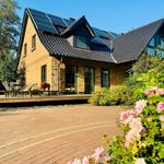 Haus mit Solaranlage, Terrasse und Blumenbeet im Vordergrund.