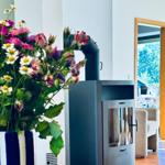 Kaminofen neben Blumenstrauß, Blick in Wohnbereich mit Sitzgelegenheit.