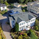 Haus mit Garten und Terrasse. Umgeben von Bäumen und weiteren Gebäuden.