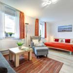 Schlafzimmer mit Bett, Sessel, Couch und Fenstern mit Vorhängen.