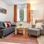 Wohnzimmer mit Sofa, Sessel und Holztisch. Fenster mit orangefarbenen Vorhängen.