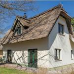 Haus mit Strohdach, grünen Fenstern und Terrasse mit Tisch und Stühlen.