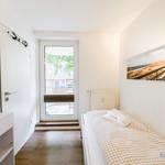 Schlafzimmer mit Bett, Tür und Fenster zur Terrasse.