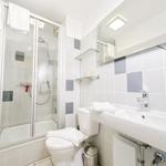 Badezimmer mit Dusche, Waschbecken und Toilette. Weiße Fliesen und Spiegelschrank.