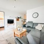 Wohnzimmer mit Sofa, Couchtisch und Fernseher. Küche und Schlafzimmer sind sichtbar.