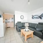 Wohnküche mit grauem Sofa, Holztisch und Küchenschränken.