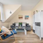 Wohnzimmer mit Sofa, Sessel und Glas-Tisch unter Dachschrägen.