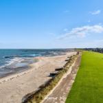 Strand mit grünem Rasen und Blick auf das Meer unter blauem Himmel.