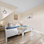 Schlafzimmer mit weißem Bett, Holzboden und Spiegeln an der Wand.