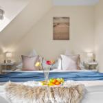 Schlafzimmer mit Dachschrägen, Bett mit Kissen und Decke, Wandbild und Nachttische mit Lampen.