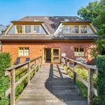 Haus mit Holzbrücke, roten Ziegel und gelben Fensterrahmen.