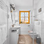 Badezimmer mit Dusche, Toilette und Waschbecken. Fenster mit Vogelmotiv.