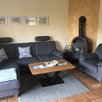 Ein Wohnzimmer mit grauem Sofa, Sessel, Holztisch und Kaminofen.