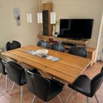 Esszimmer mit Holztisch, sechs Stühlen, Fernseher und Fenster.