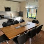 Essbereich mit Holztisch und sechs Stühlen. Küchenzeile mit Einbauküche und Fenster.