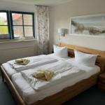 Zimmer mit Doppelbett, Fenster und Strandbild an der Wand.