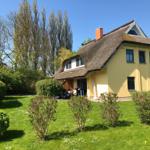Haus mit Strohdach und Garten. Terrasse mit Tisch und Stühlen.