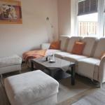 Wohnzimmer mit Sofa, Hocker und Tisch. Fenster mit Jalousie und Wandbild.