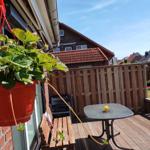 Terrasse mit Tisch, Stuhl und hängender Pflanze. Holzgeländer und Garten im Hintergrund.