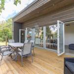 Terrasse mit Tisch, Stühlen und Grill. Durchgehende Glastüren führen ins Haus.