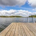 Holzsteg führt zum Wasser, Boot liegt bereit, Blick auf den See und grüne Ufer.