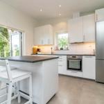 Moderne Küche mit weißer Arbeitsplatte, Edelstahlkühlschrank und Blick auf den Garten.