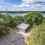 Hütte mit Blick auf See und Wald. Gravelweg und Bäume umgeben das Haus.
