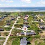 Luftbild von Ferienhäusern an der Küste mit grünen Dünen und Meer im Hintergrund.