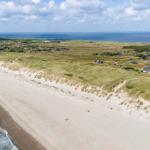 Strand mit Dünen und Häusern am Meer unter blauem Himmel.