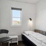 Schlafzimmer mit Bett, Stuhl und Fenster. Wandlampe und Bilder an der Wand.