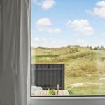 Durch das Fenster blickt man auf eine grüne Dünenlandschaft unter blauem Himmel.