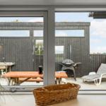 Terrasse mit Grill, Liegestuhl und Holztisch. Blick auf dunkle Holzwände und Himmel.