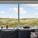 Ein Fenster mit Blick auf Dünenlandschaft. Auf dem Sims stehen ein Krug, eine Schale und ein Schuh.