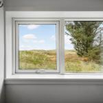 Durch das Fenster blickt man auf eine grüne Landschaft mit einem Baum.