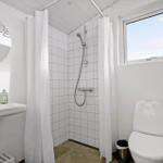 Badezimmer mit Dusche, Toilette und Waschbecken. Fenster und Spiegel sichtbar.