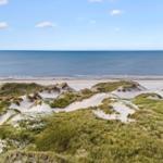 Weitläufiger Blick auf Strand und Meer mit Dünen im Vordergrund.