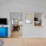 Wohnbereich mit TV, Essbereich und Küche sichtbar. Holzfußboden und weiße Wände.