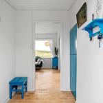 Flur mit blauem Hocker und Schrank. Durchgang in Wohnzimmer mit Blick auf Dünenschlucht.