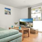 Wohnzimmer mit Sofa, TV und Fenster zur Terrasse.