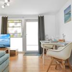 Wohn- und Essbereich mit Fernseher, Tisch, Stühlen und Balkontür.