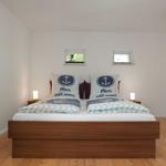 Schlafzimmer mit Bett, zwei Nachttischen und zwei kleinen Fenstern.