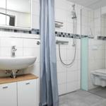 Badezimmer mit Dusche, Toilette und Waschbecken auf Holzunterschrank.