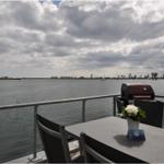 Terrasse mit Grill und Tisch am Wasser mit Blick auf See und Segelboot.