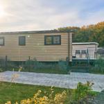 Moderne Holzhütte mit Terrasse, Grill und Gartenbereich. Sonniger Tag mit Wald im Hintergrund.