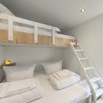 Zimmer mit Doppelbett und Hochbett mit Leiter und Fenster.